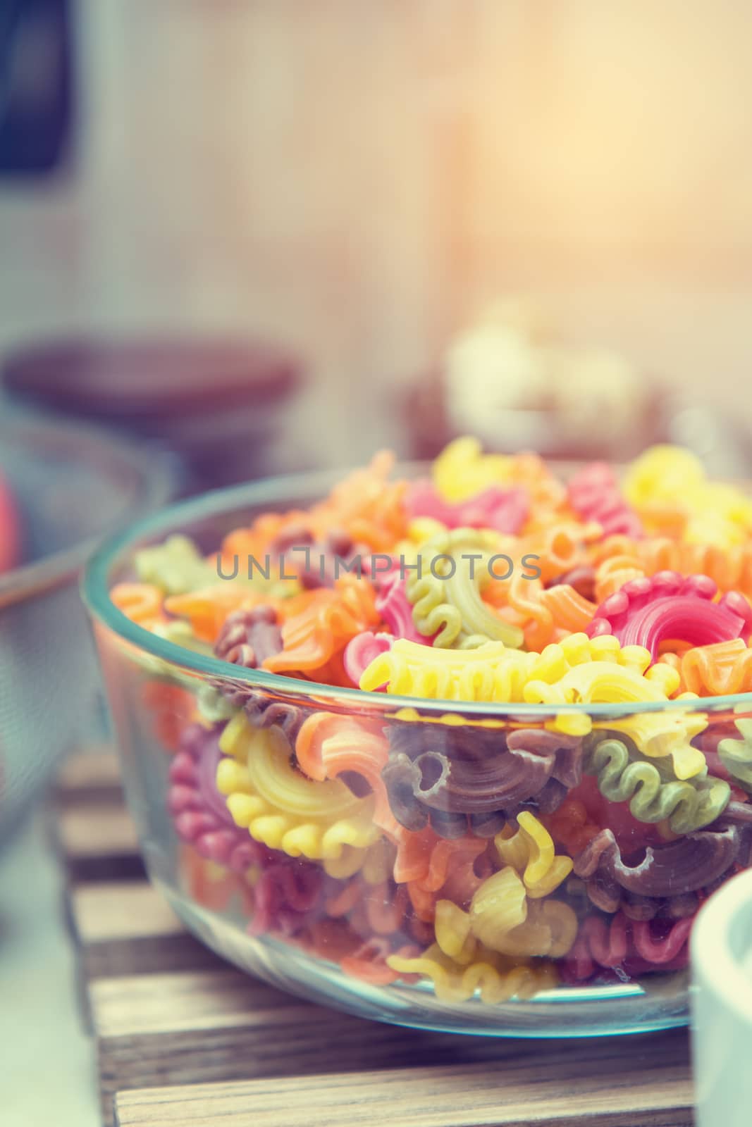 Raw multicolor creste di gallo pasta crude shells macaroni in glass bowl in a modern kitchen. Shallow depth of field. Toned