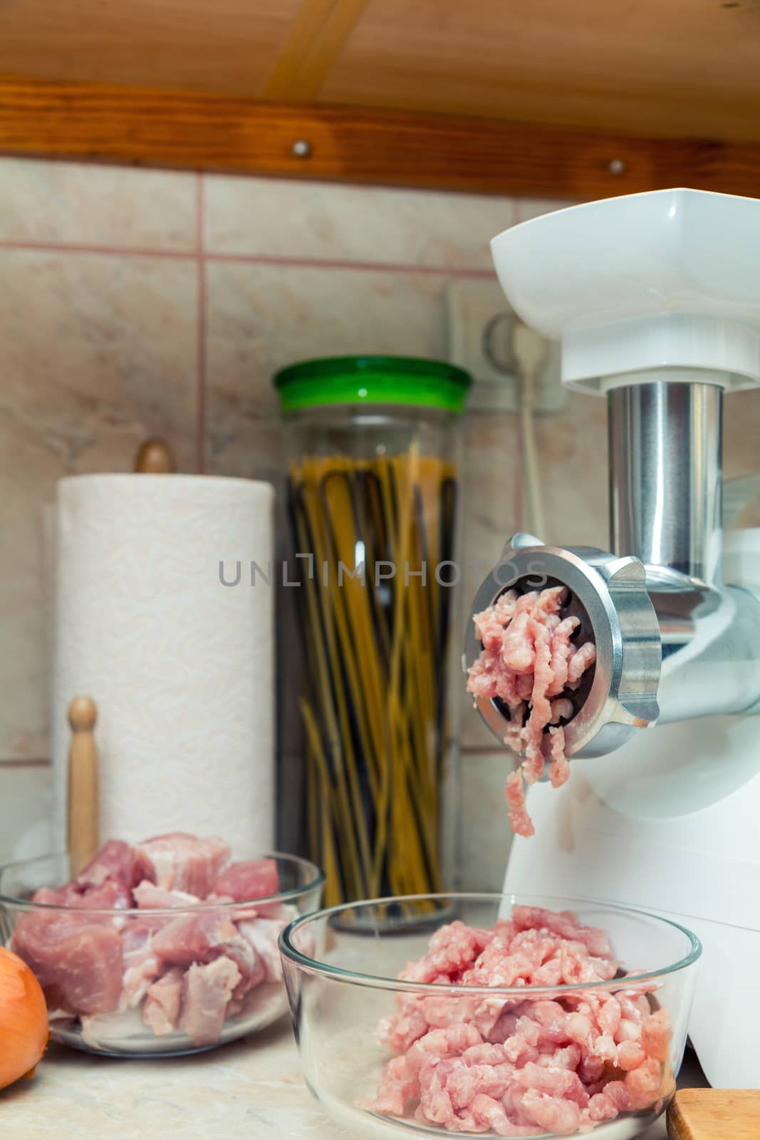 Home electric meat-grinder is making pork stuffing in a modern kitchen. Pork stuffing in a glass bowl.