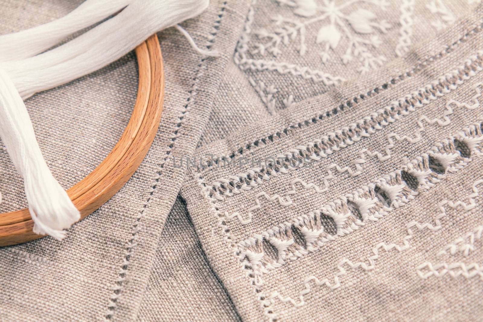 Set for embroidery. Embroidery thread white color, embroidery hoop and needle on linen with needlework in progress. Coloring and processing photos. Shallow depth of field.