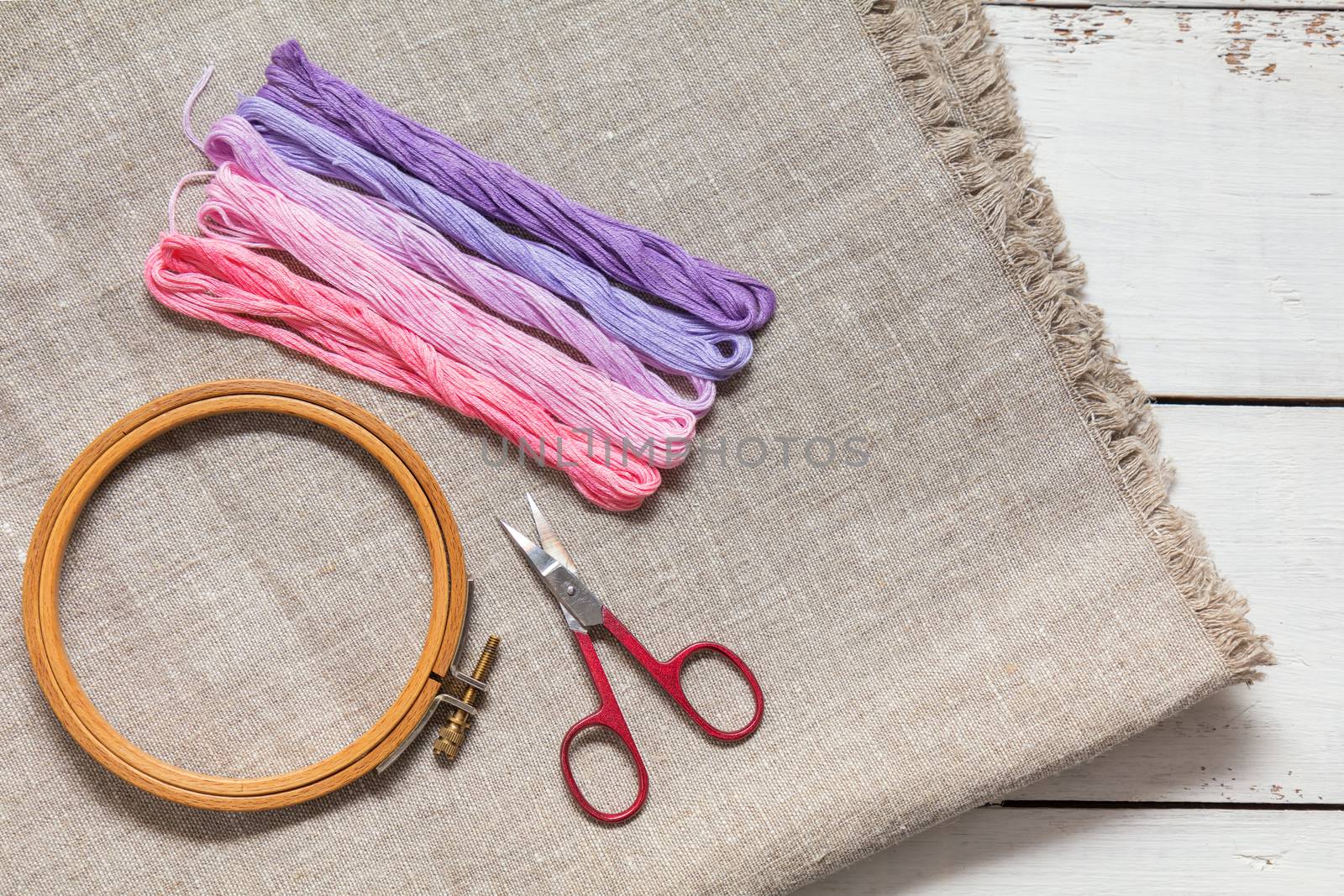 Set for embroidery. Embroidery thread shades of violet and pink color, embroidery hoop, scissors and needle on linen homespun cloth. Coloring and processing photos. Shallow depth of field.