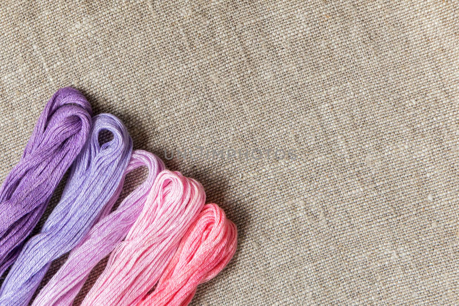 Set for embroidery. Embroidery thread shades of violet and pink color on linen homespun cloth. Coloring and processing photos. Shallow depth of field.