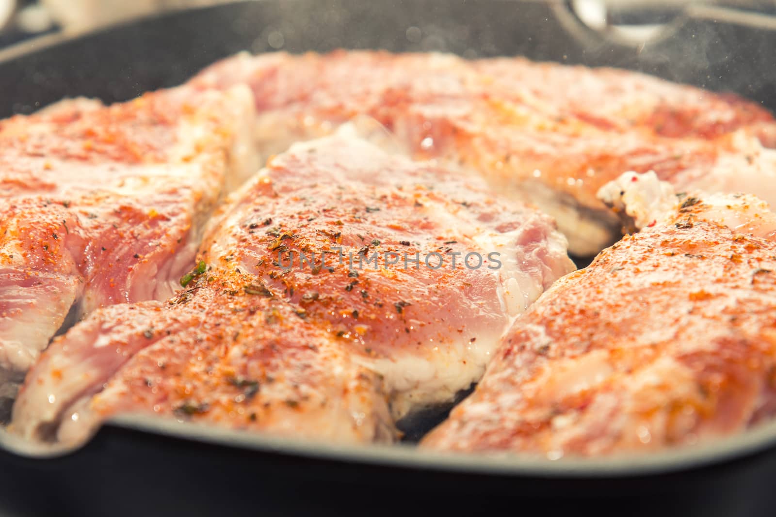 Fresh pork steak with spices cooking on teflon pan grill. Shallow depth of field.