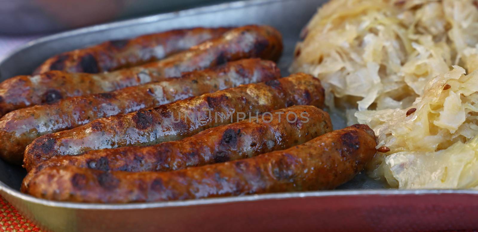 Close up portion of grilled Nuremberg Bratwurst sausages with side dish of sauerkraut on metal pewter plate, low angle view
