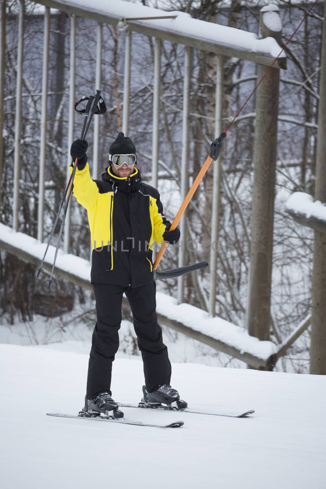 Happy smiling male skier using t bar ski drag lift and greeting waving his ski poles