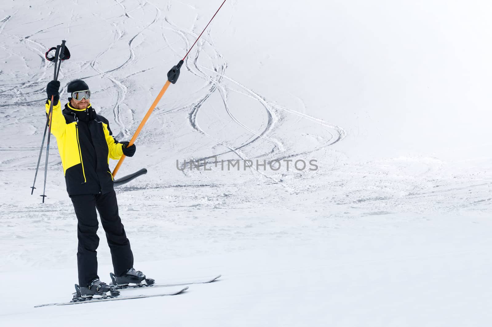 Happy smiling male skier using t bar ski drag lift and greeting waving his ski poles