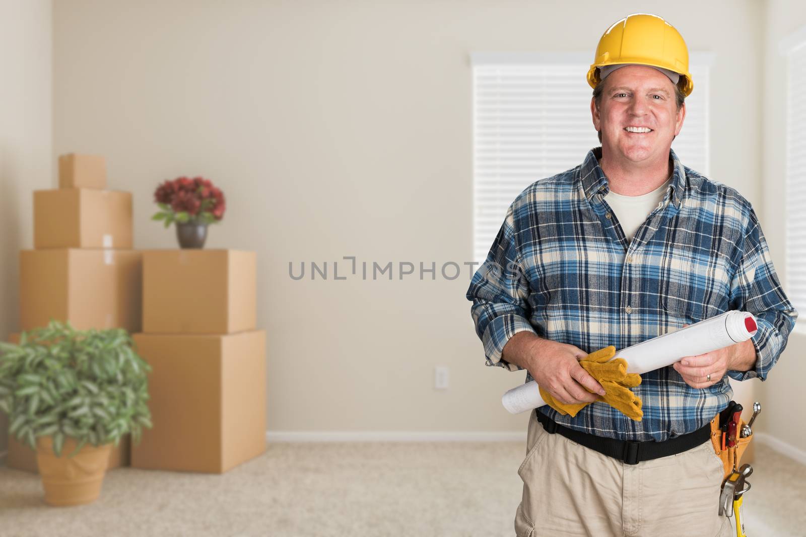 Contractor With Plans and Hard Hat Inside Empty Room with Moving Boxes. by Feverpitched