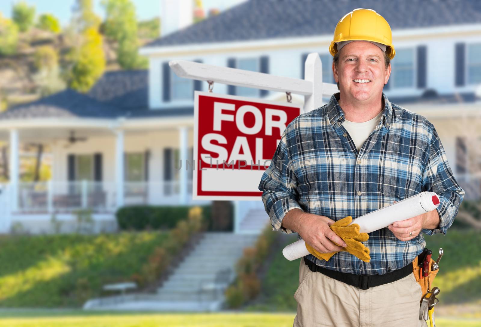 Contractor With Plans and Hard Hat In Front of For Sale Real Estate Sign and House. by Feverpitched