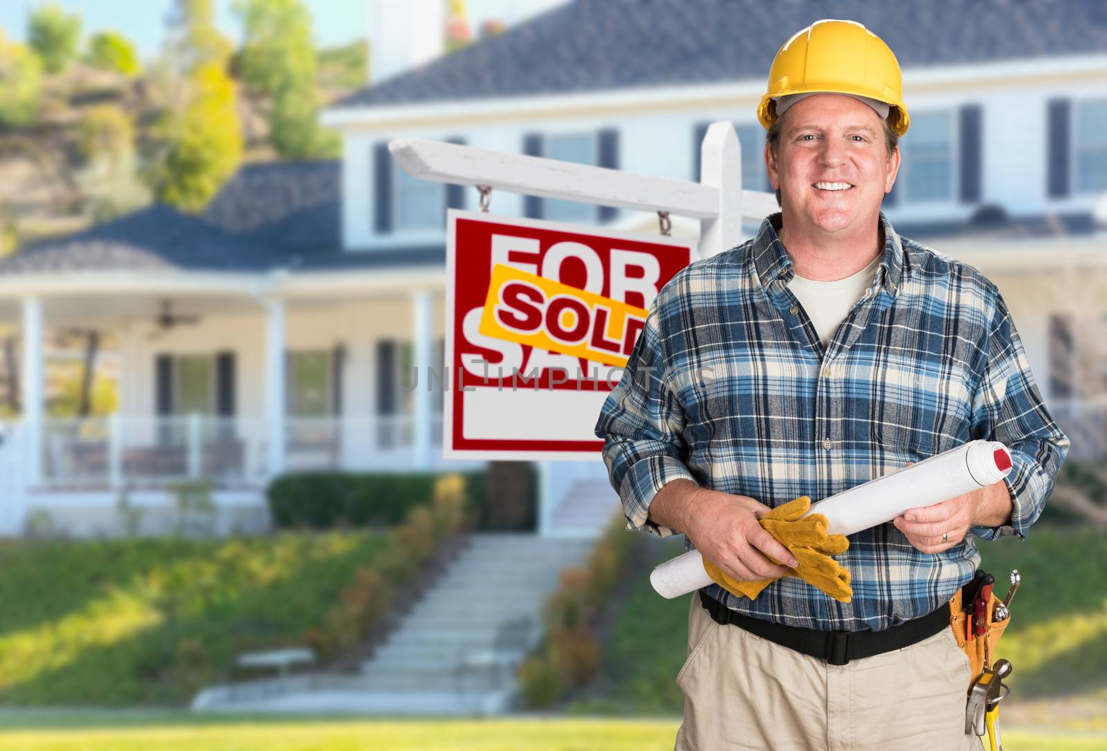 Contractor With Plans and Hard Hat In Front of Sold For Sale Real Estate Sign and House.