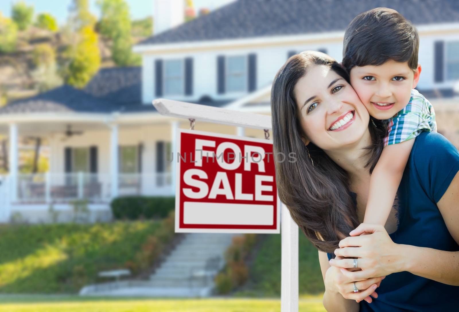 Young Mother and Son In Front of For Sale Real Estate Sign and House.