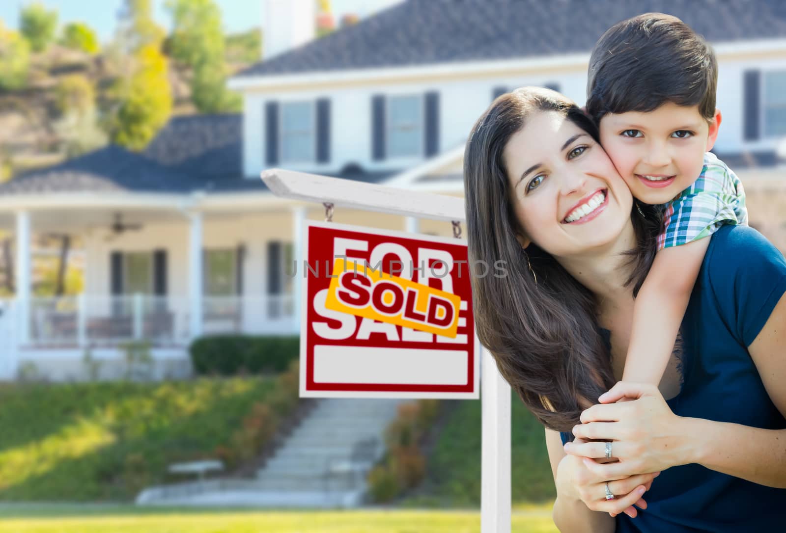Young Mother and Son In Front of Sold For Sale Real Estate Sign and House.