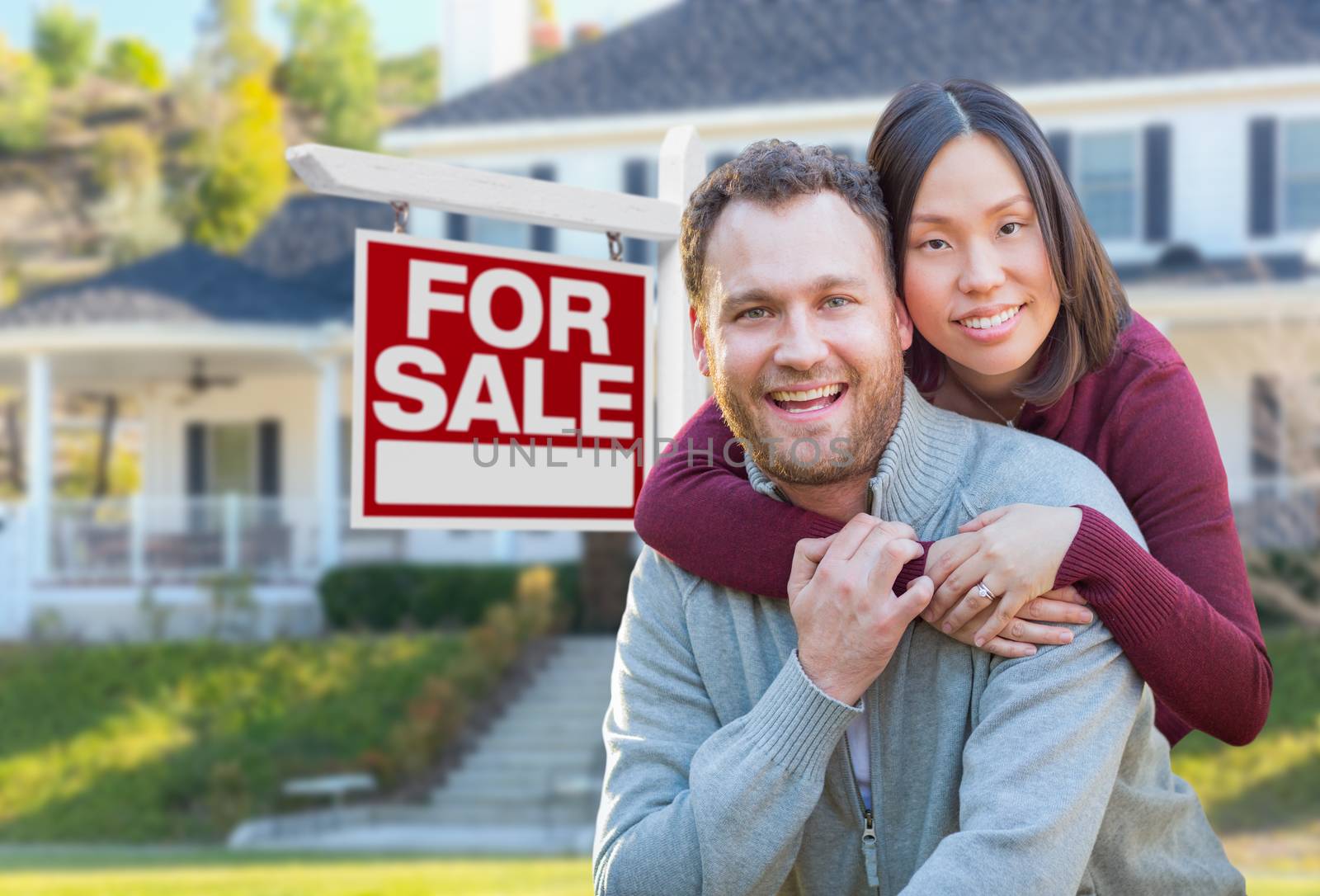 Mixed Race Caucasian and Chinese Couple In Front of For Sale Real Estate Sign and House.