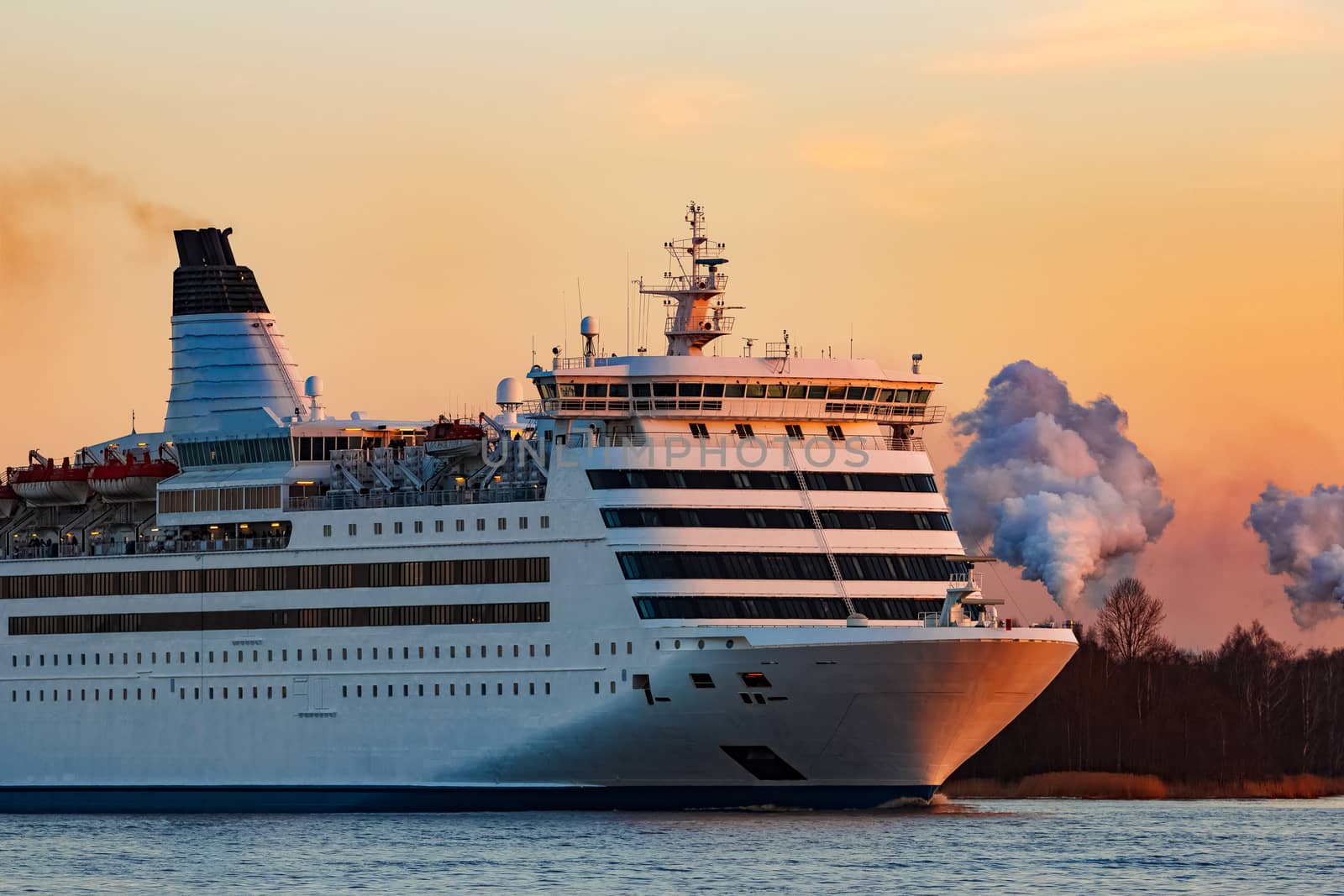 White passenger ship moving against the orange sunset sky