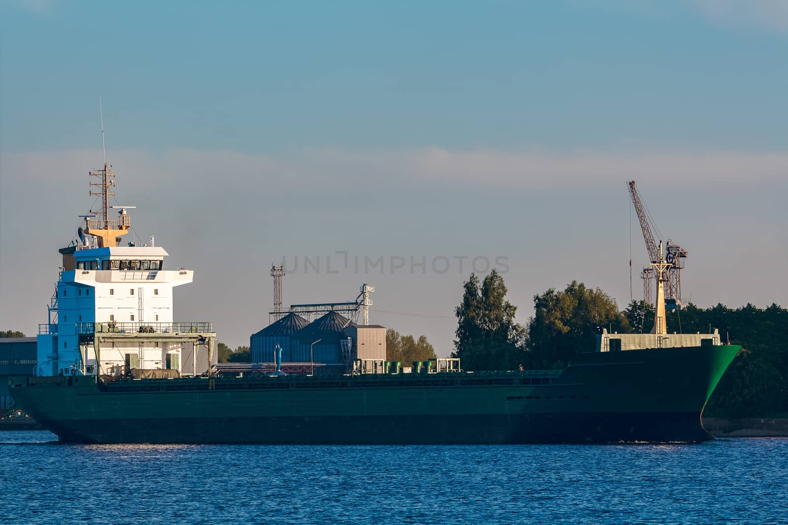 Green cargo ship leaves the port in a clear day