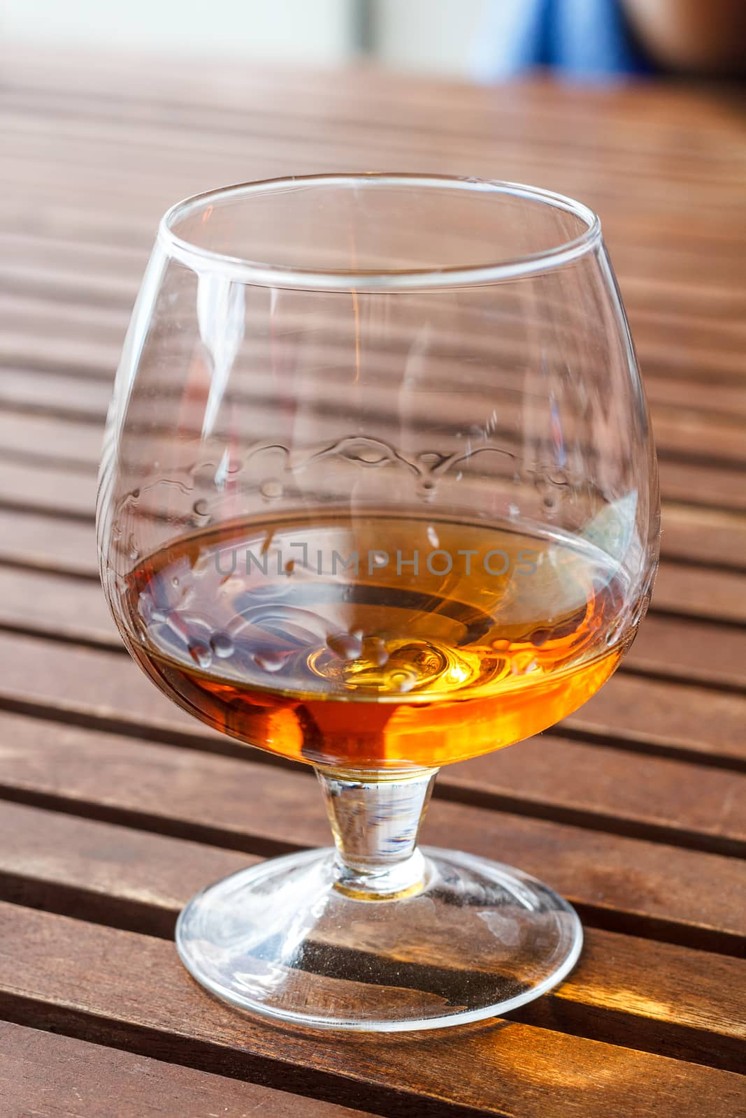 Glass of cognac standing on a wooden table in sunlight.
