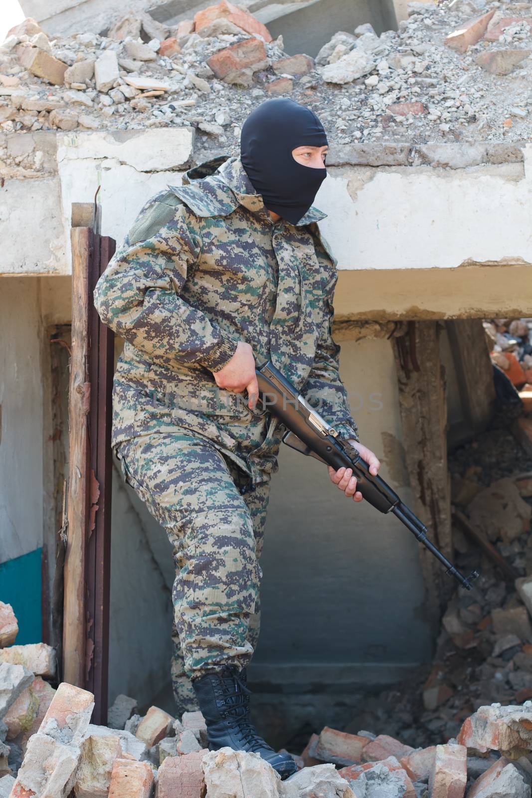 Military camouflage with a rifle on a background of bombed buildings.