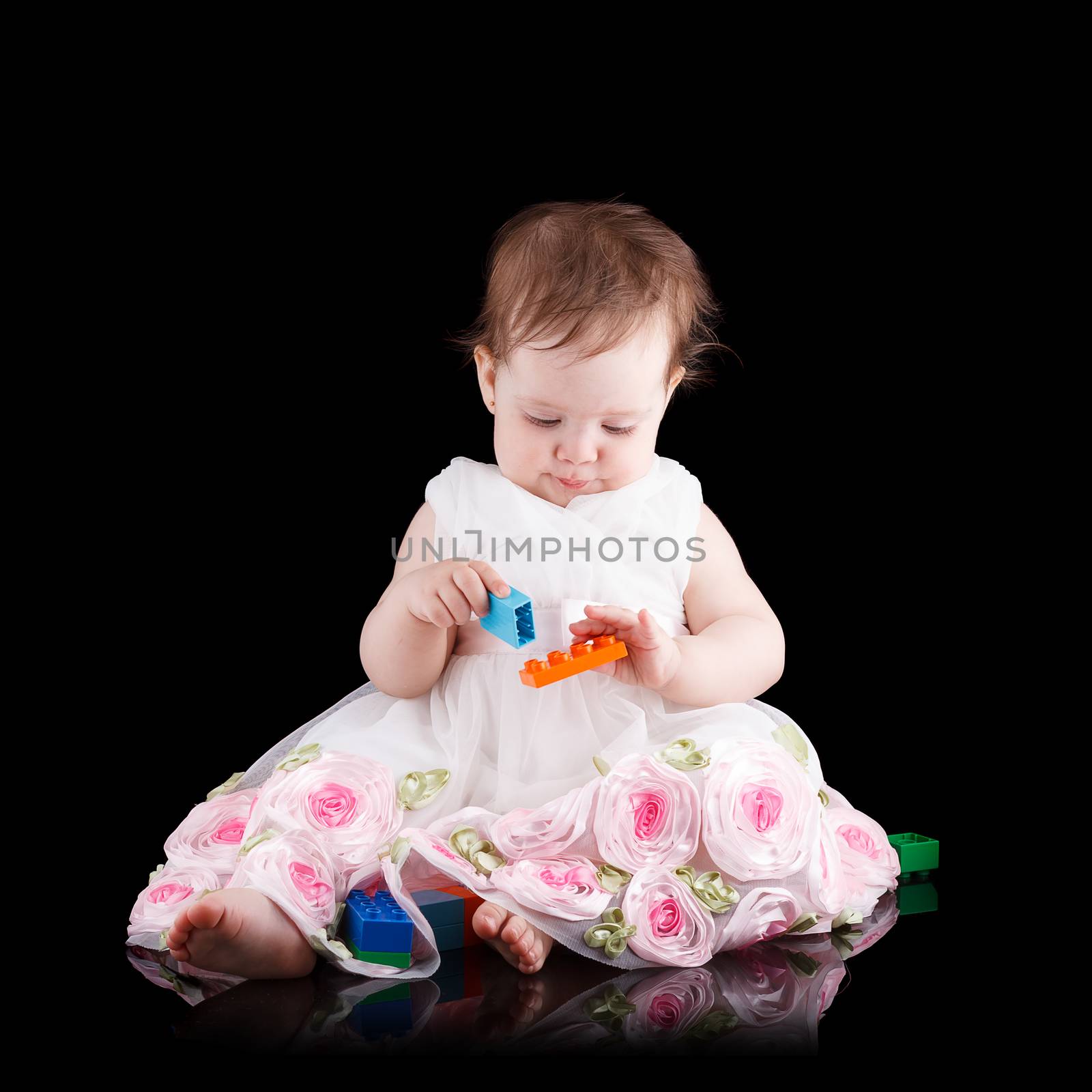 The girl is one year in dress sitting on a black background.