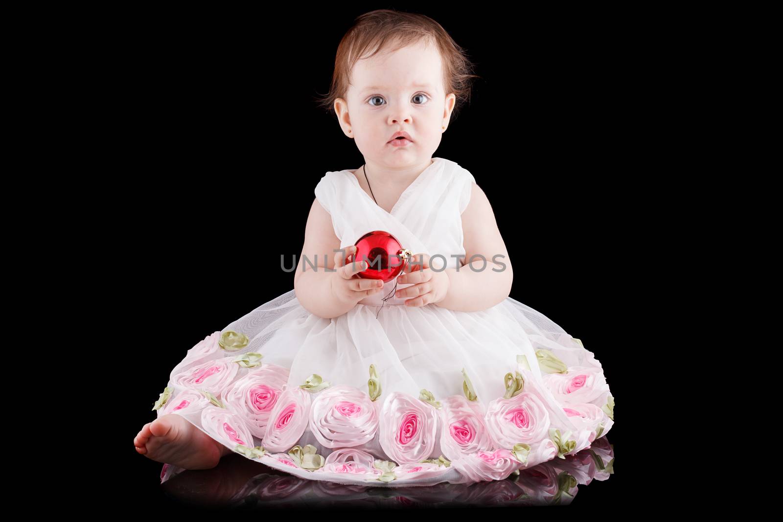 The girl is one year in dress sitting on a black background.