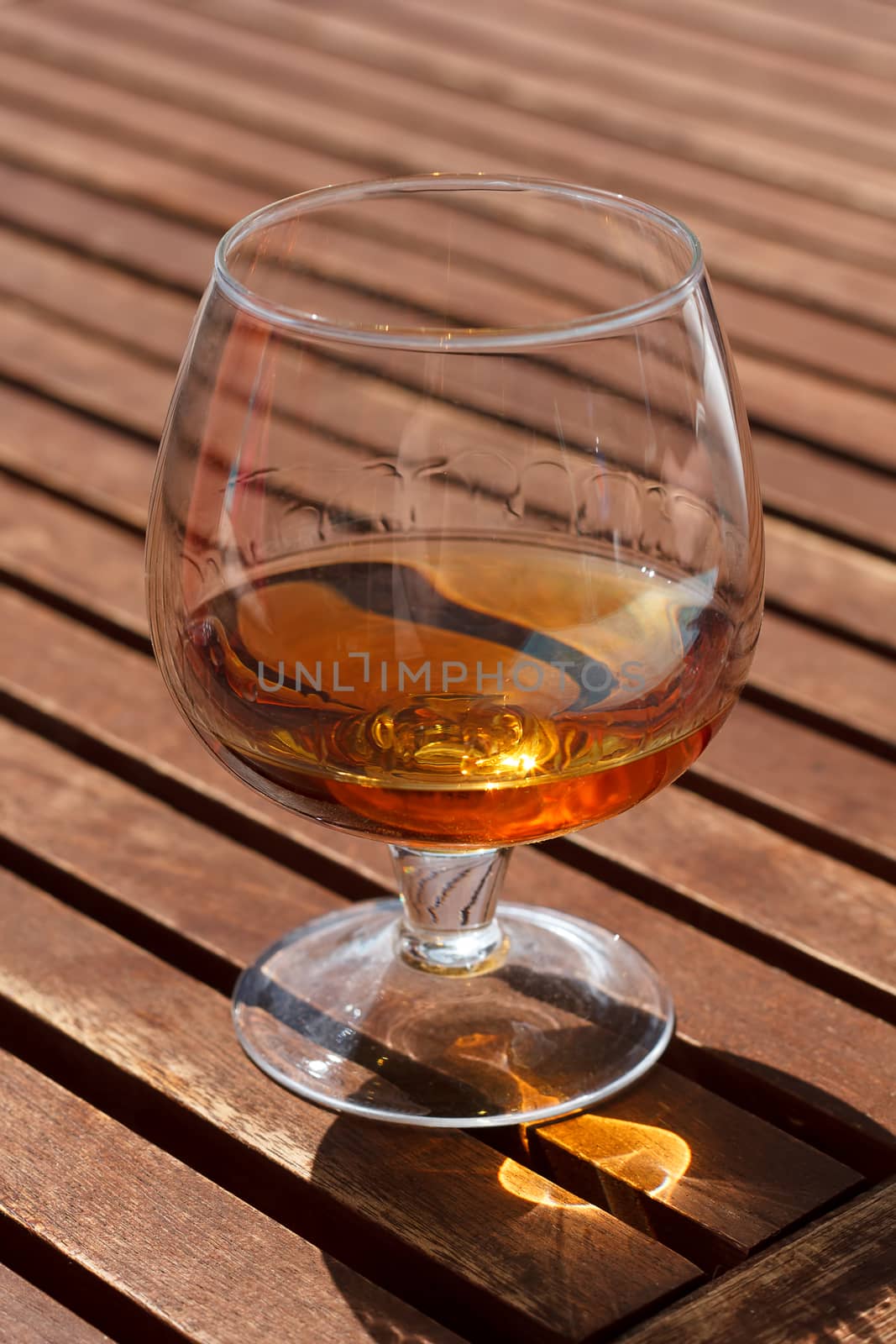 Glass of cognac standing on a wooden table in sunlight.