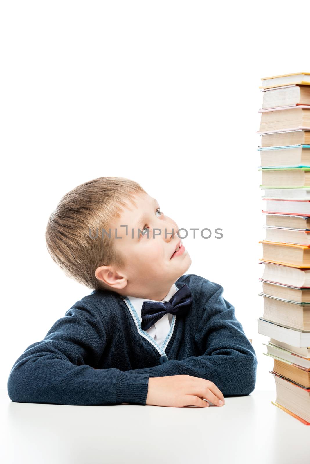 the schoolboy looks at the heap of books on the table