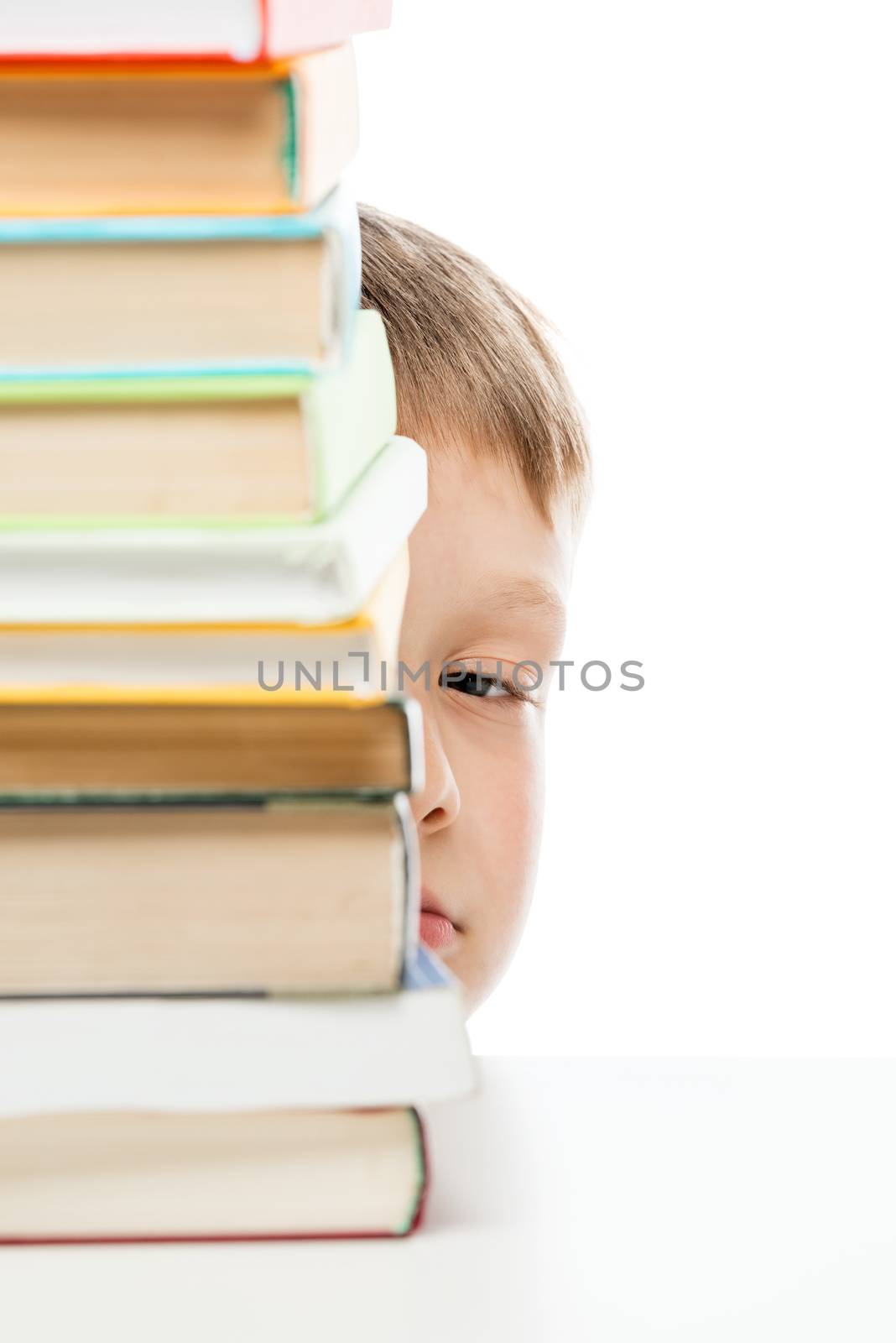 pile of books to read on the table and peeping out from behind the books the schoolboy