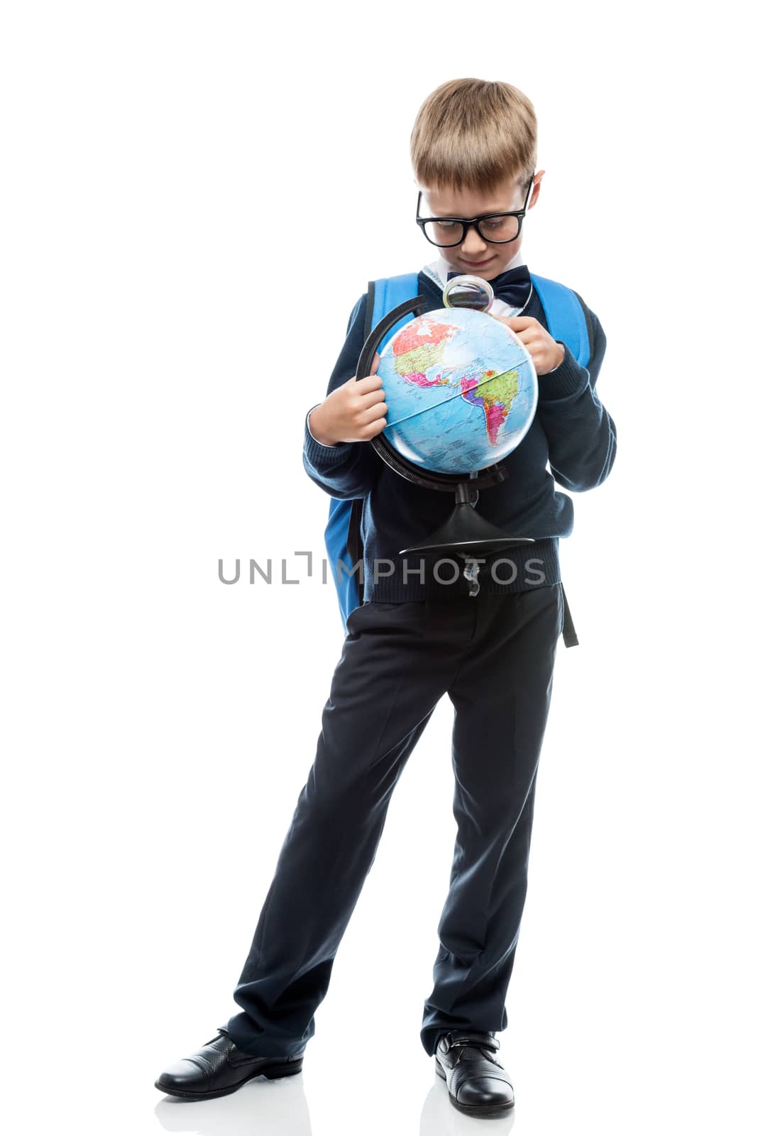 schoolboy examines through magnifier glass globe, portrait is isolated in full length on a white background