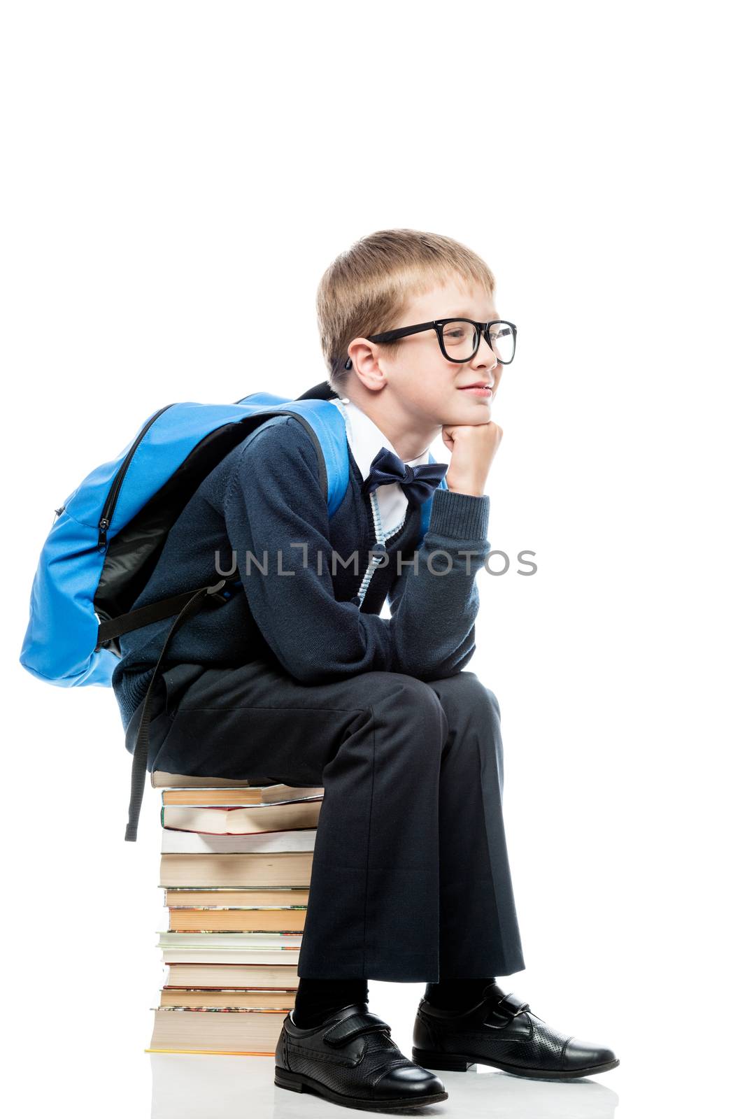 thoughtful schoolboy sitting on a pile of books on a white background