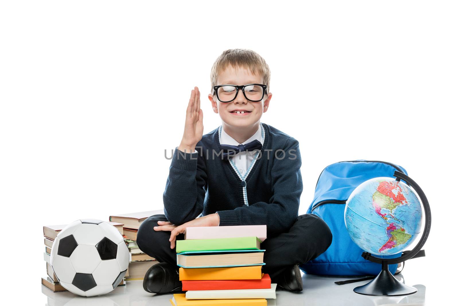 schoolboy 8 years old with a raised hand for the answer of the lesson, sits on a white background with books