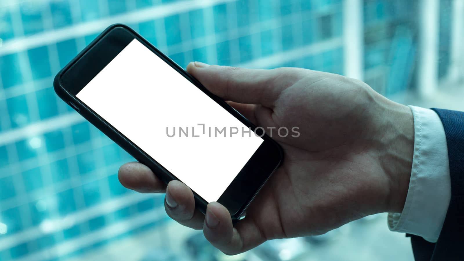 Businessman is holding black smartphone with white screen near the window in office