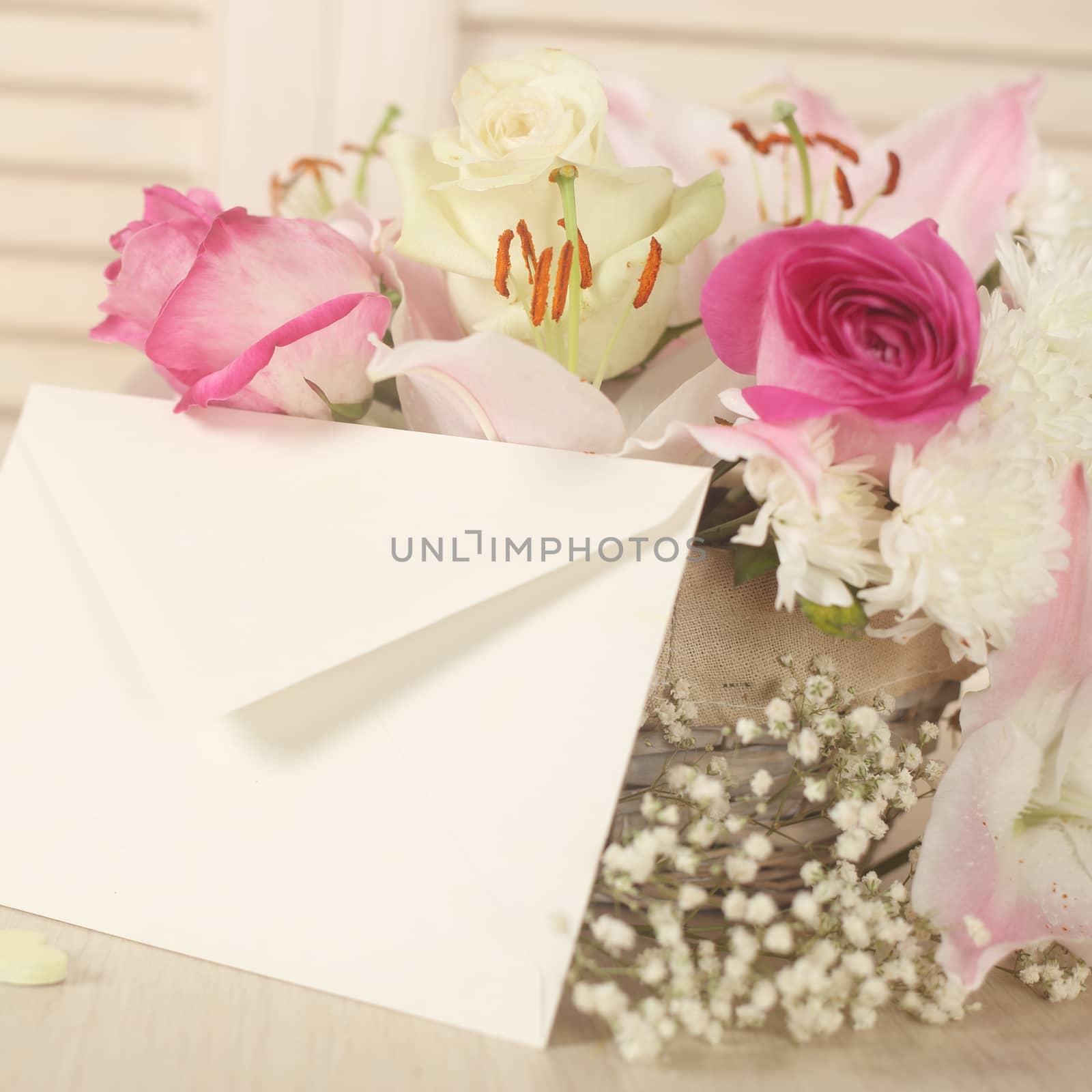 Basket of flowers and blank envelope on wooden background