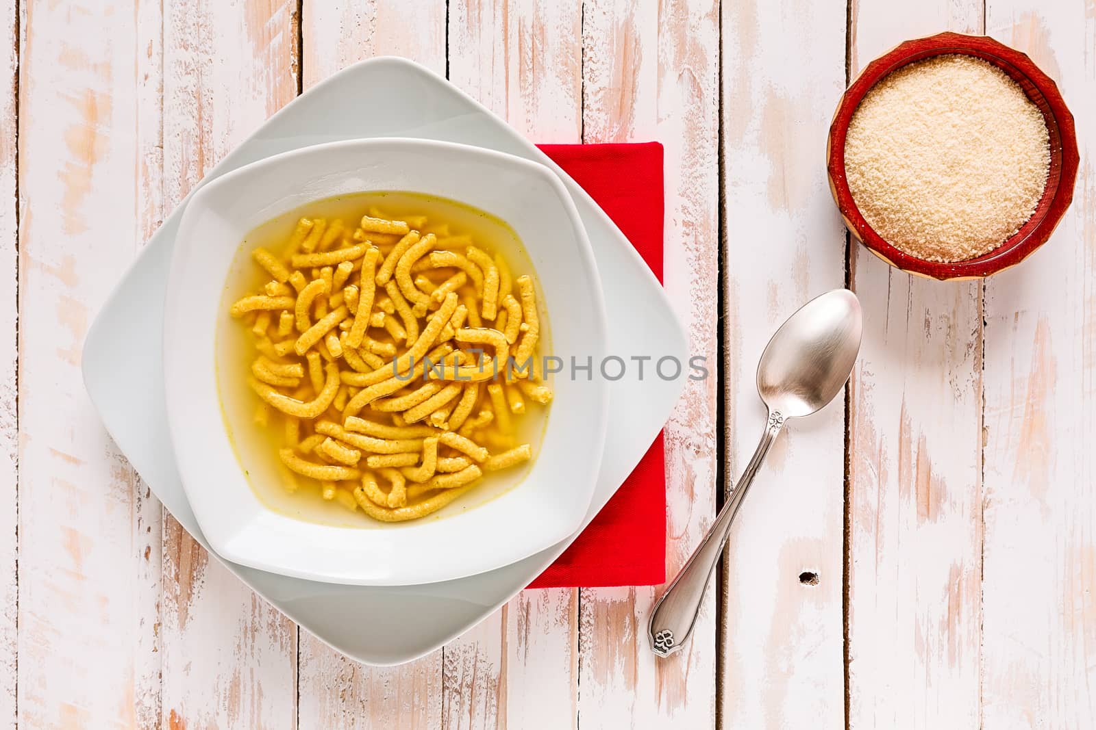 Italian passatelli in broth over a wooden table seen from above