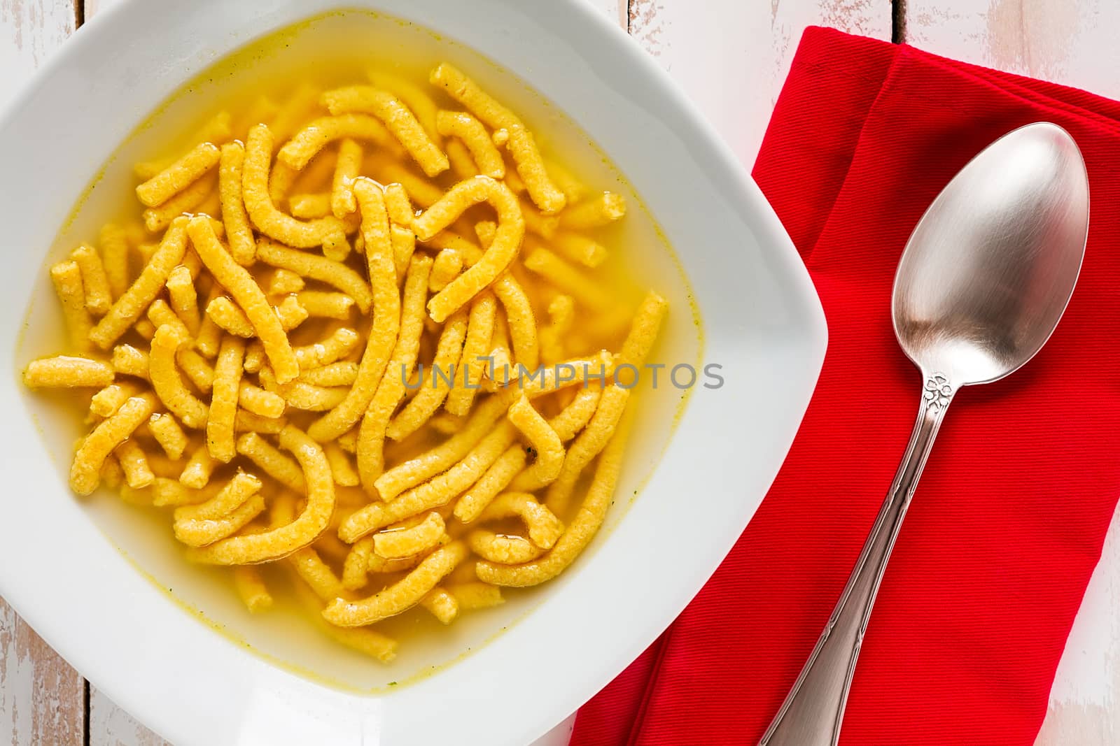 Closeup of Italian passatelli in broth over a wooden table seen from above
