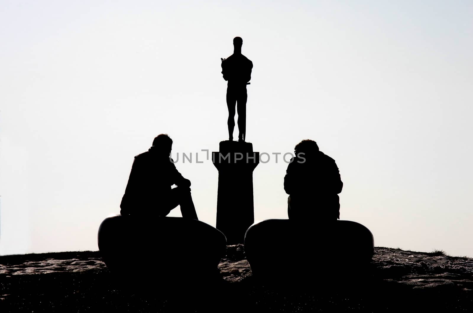 Two men sitting in front of statue of Pobednik in Belgrade at sunset