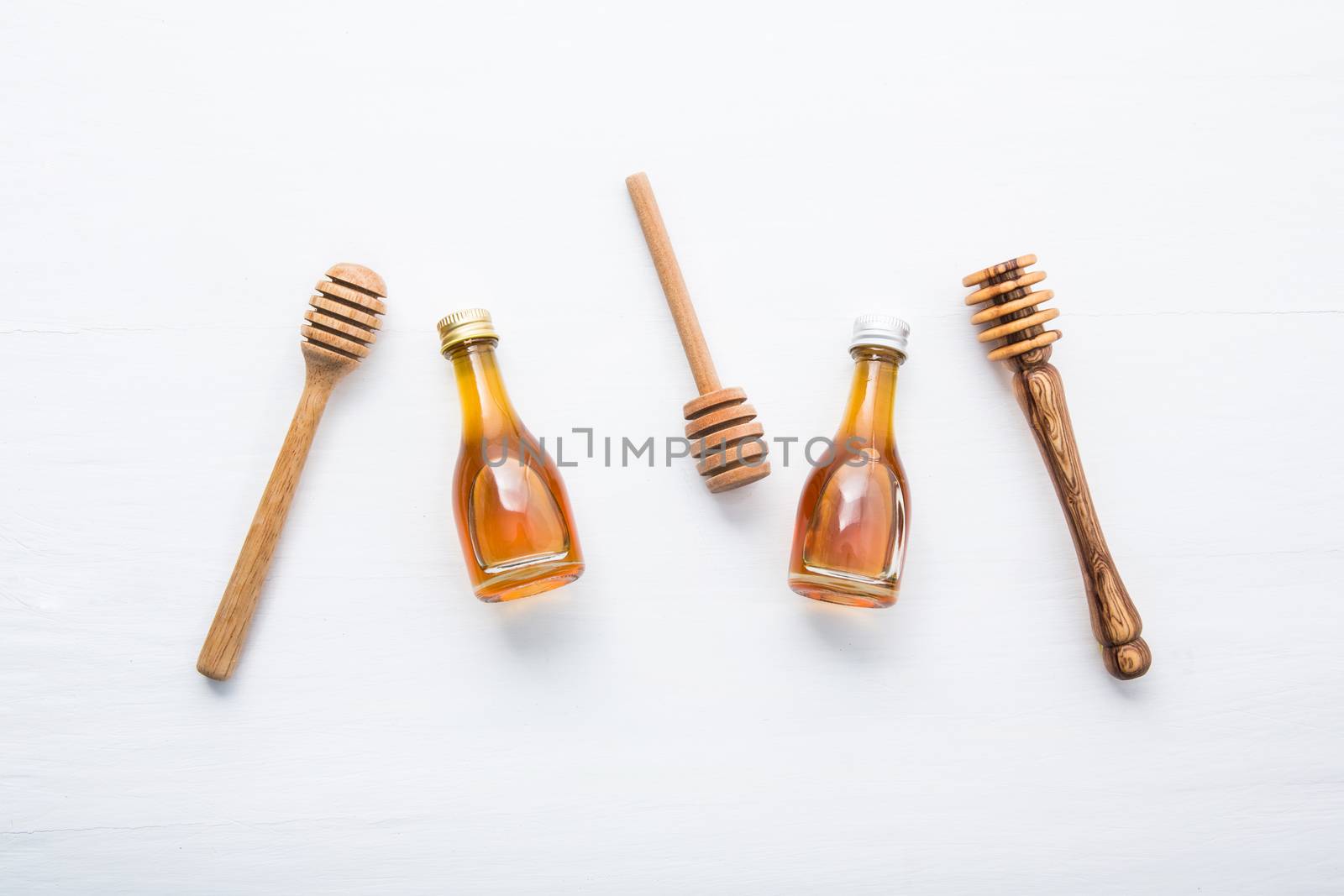 Honey wooden dipper and little honey bottle on white wooden background.