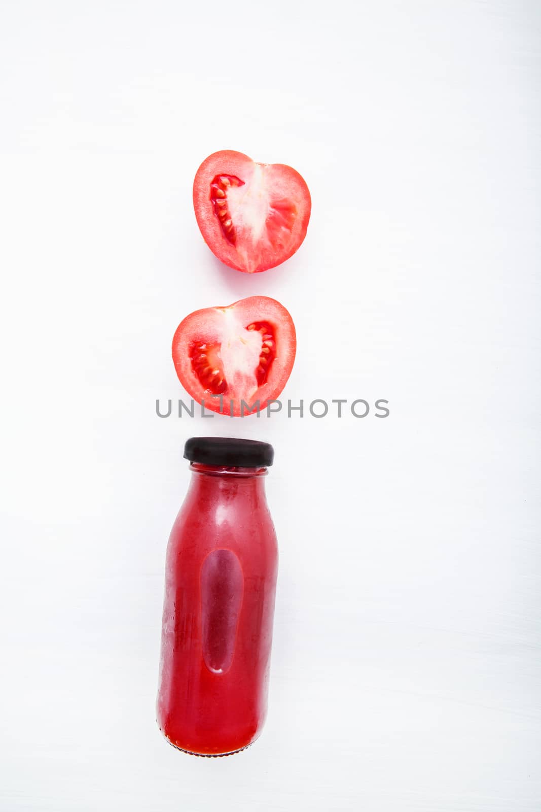 Tomatoes juice in bottle and fresh tomatoes slices on white wooden background.