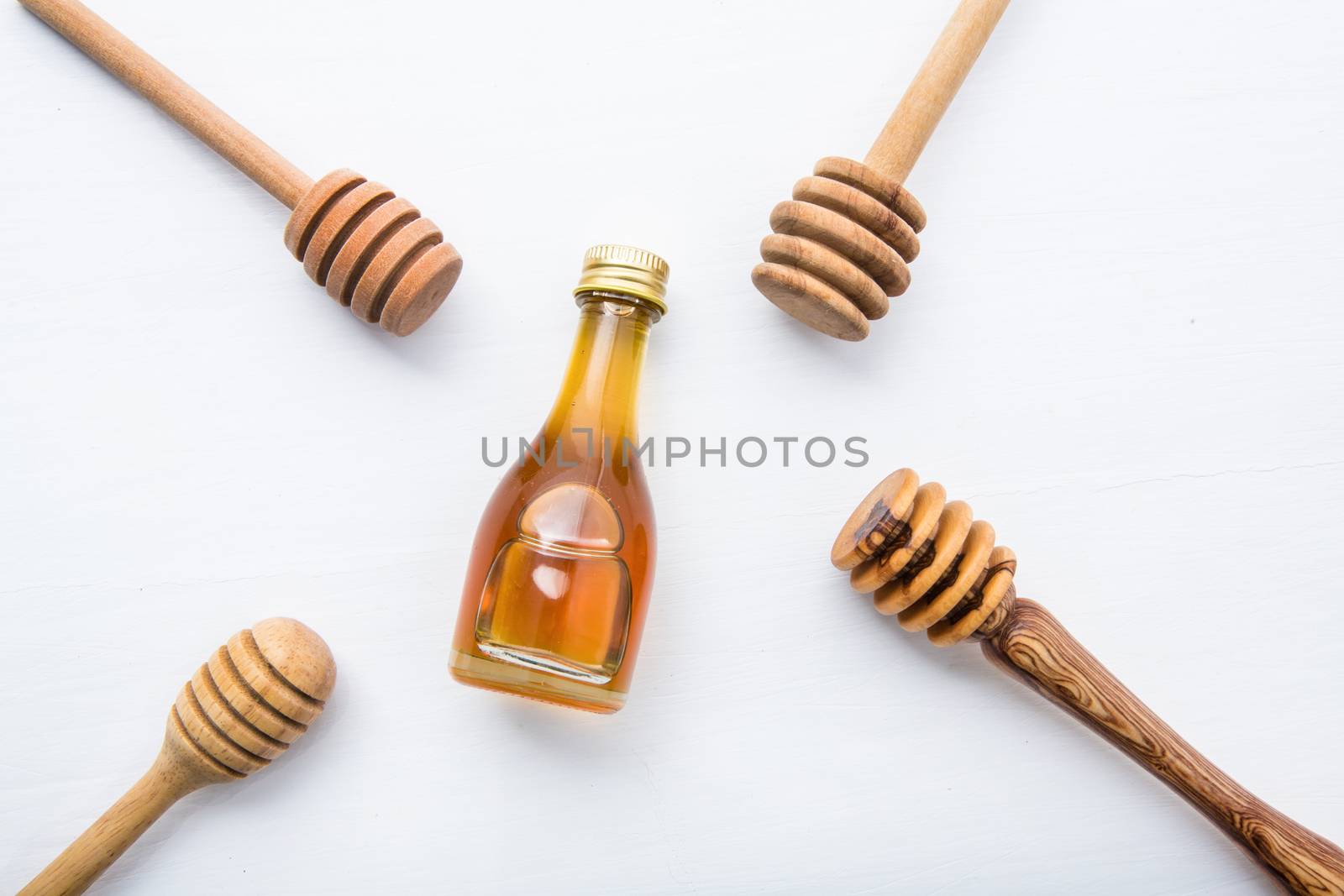 Honey wooden dipper and little honey bottle on white wooden background.