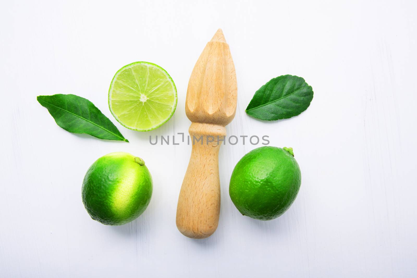 Fresh limes and wooden juicer on white background. Top view with copy space