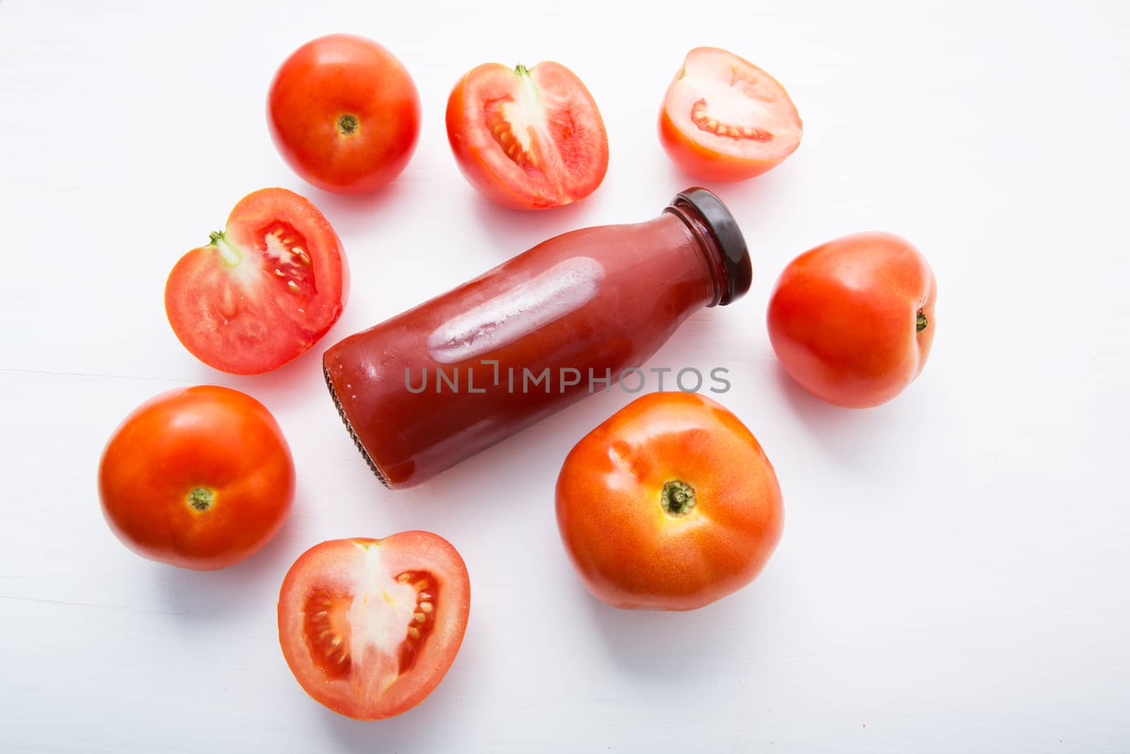 Fresh tomatoes juice in bottle and fresh tomatoes slices on white wooden background.