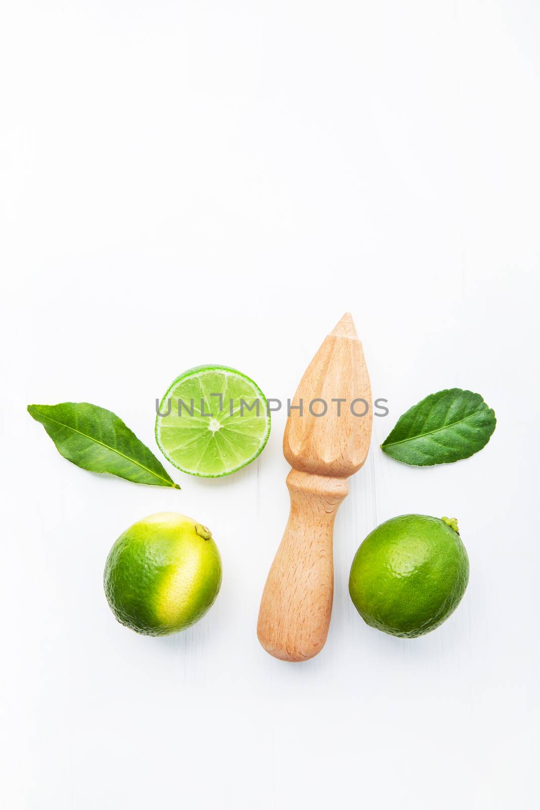 Fresh limes and wooden juicer on white background. Top view with copy space