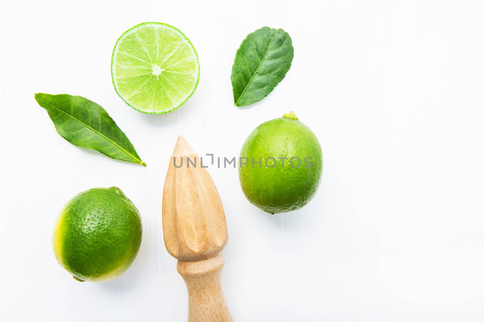 Fresh limes and wooden juicer on white background. Top view with copy space