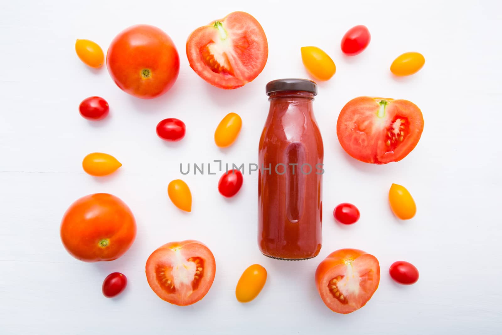 Tomatoes juice in bottle and fresh tomatoes slices on white wooden background.