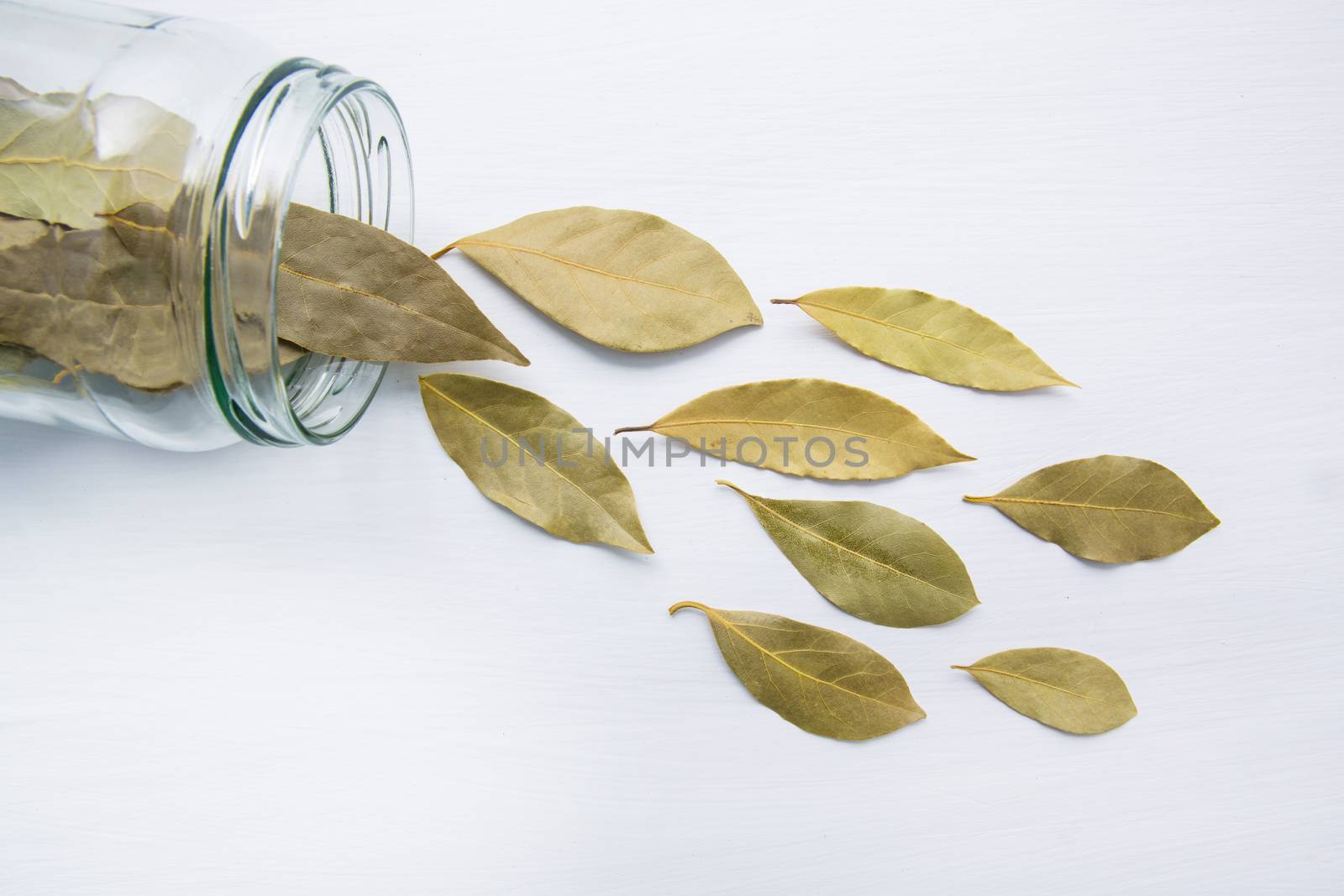 Dried bay leaves in glass jar on white wooden background.