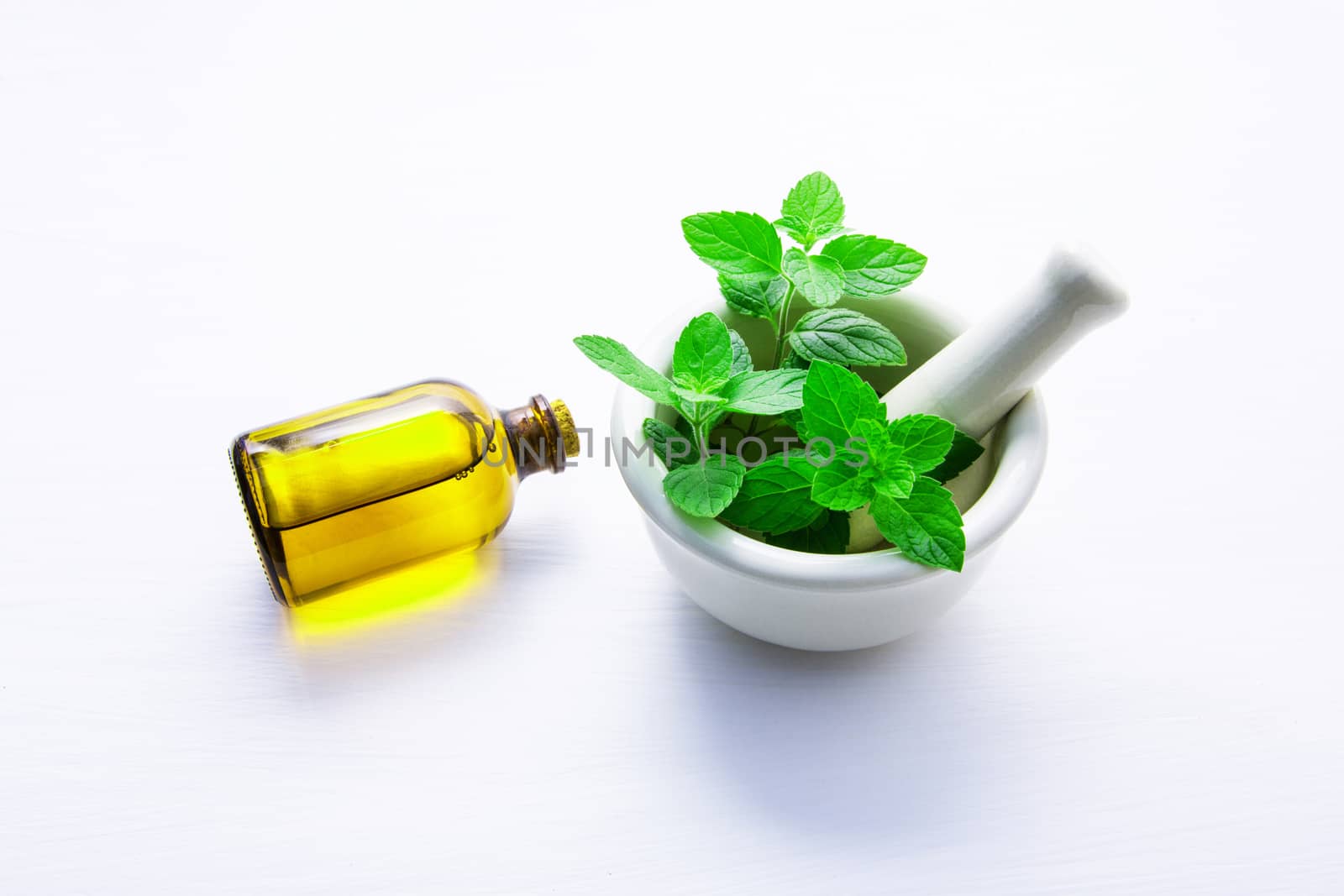 Natural Mint Essential Oil in a Glass Bottle with Fresh Mint Leaves in white porcelain mortar on white wooden background.