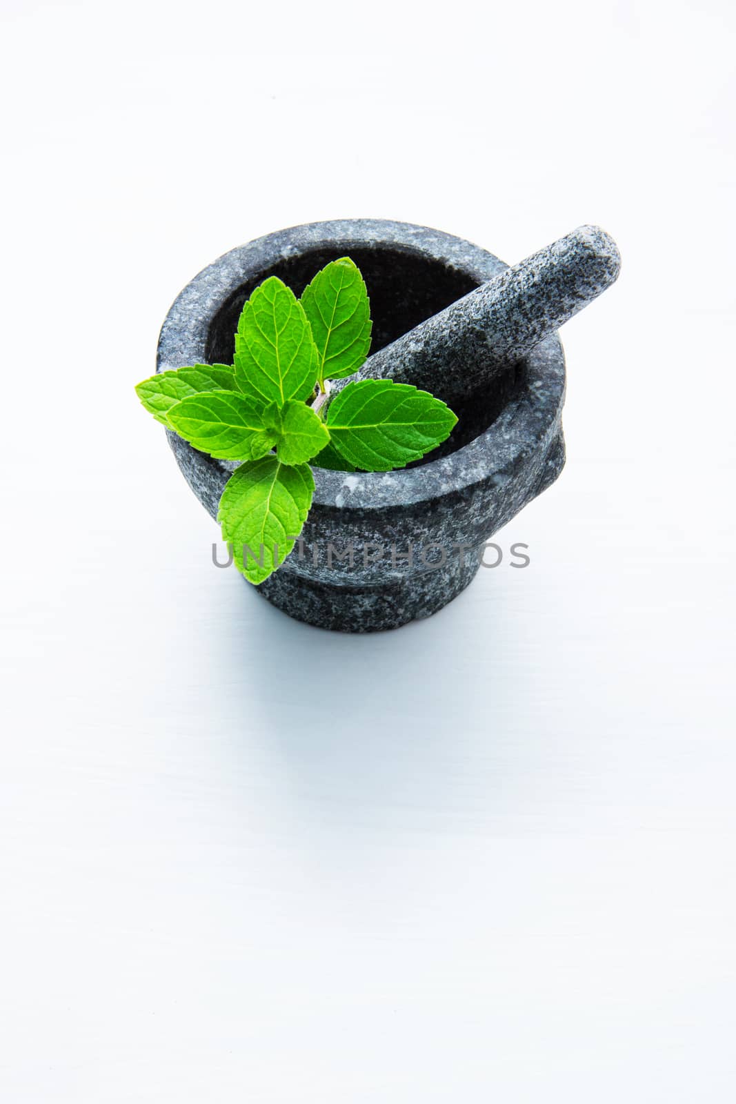 Stone mortar and pestle with peppermint leaf on white wooden bac by Bowonpat