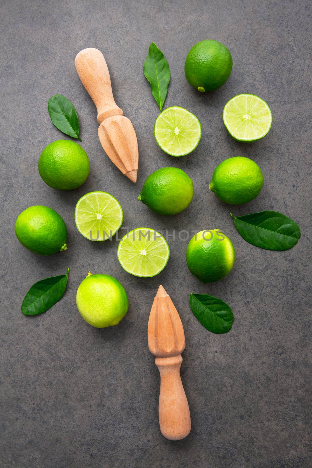 Fresh limes and wooden juicer on dark stone background. Top view by Bowonpat