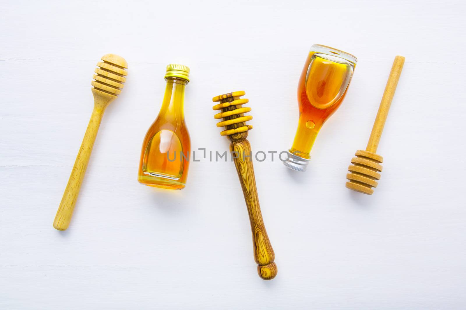 Honey wooden dipper and little honey bottle on white wooden background.