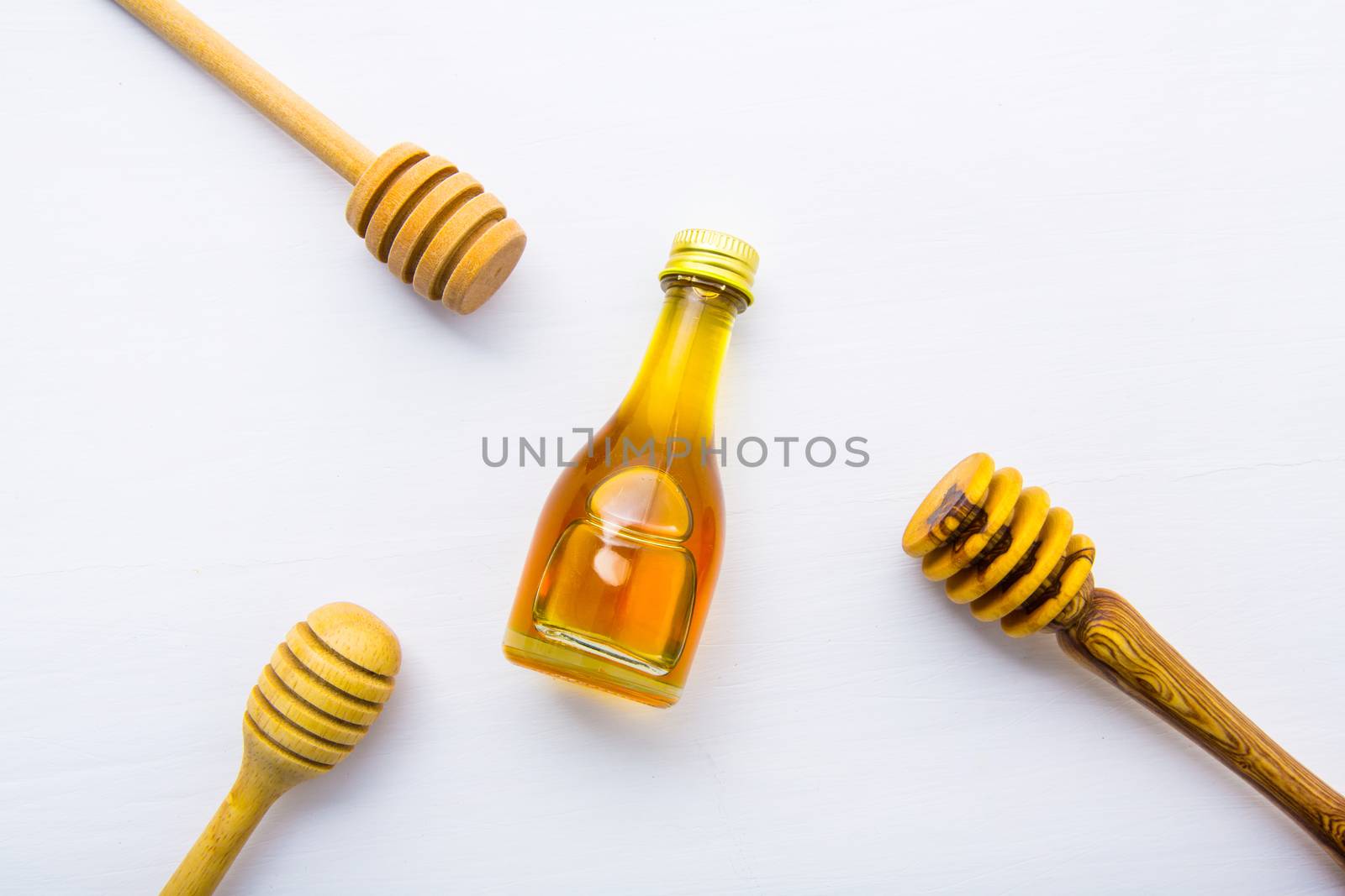 Honey wooden dipper and little honey bottle on white wooden background.