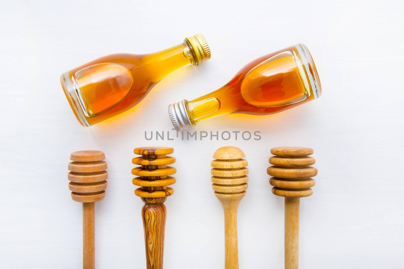 Honey wooden dipper and little honey bottle on white wooden background.