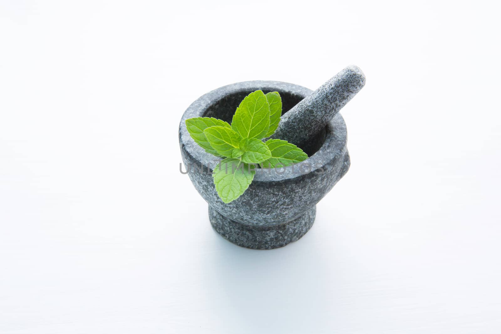 Stone mortar and pestle with peppermint leaf on white wooden bac by Bowonpat