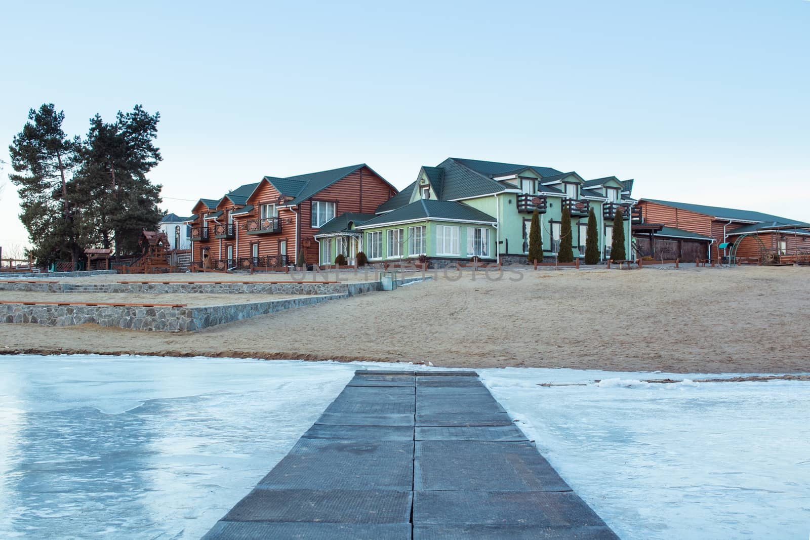 Winter village house on sandy beach near cold frozen river lake