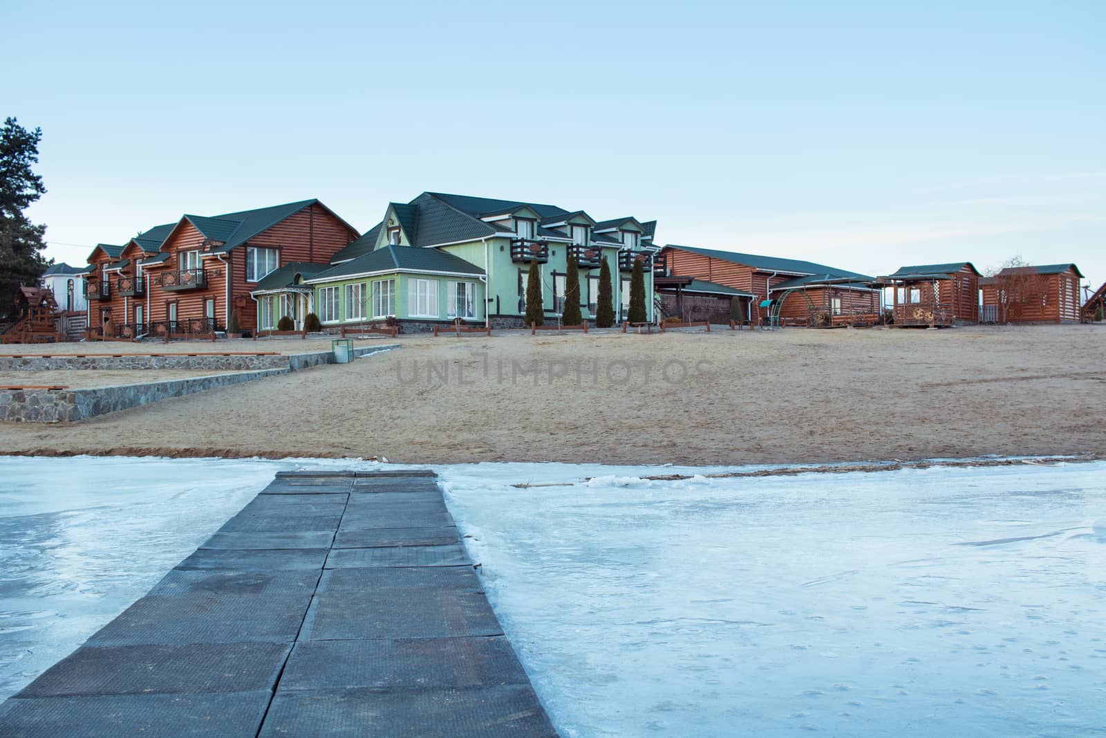 Winter village house on sandy beach near cold frozen river lake